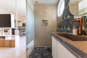 A modern bathroom with a geometric tile pattern, a glass shower enclosure, and a vanity with a sink. - Utopía 3.East-Charming Loft•Wi-Fi•AC•SelfCheck In (Medellín)