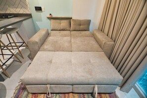 A room with a sofa bed, a small table with a plant, and a window with curtains. - Utopía 3.East-Charming Loft•Wi-Fi•AC•SelfCheck In (Medellín)