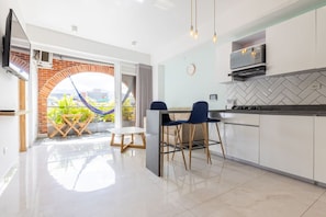 A modern kitchen with a dining area, a TV mounted on the wall, and a view of a garden through an open archway. - Utopia 5.West - Bright 2BR•AC•Self Check-In•Wi-Fi (Medellín)