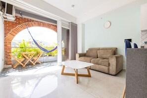 A living room with a sofa, a table, a hammock, and a view through a glass door. - Utopia 5.West - Bright 2BR•AC•Self Check-In•Wi-Fi (Medellín)