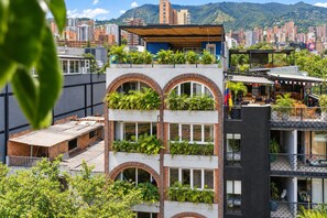 A multi-story building with balconies, some with plants, and a view of a cityscape with buildings and hills in the background. - Utopía M.East-Peacefull Loft•Wi-Fi•Self Check-In (Medellín)