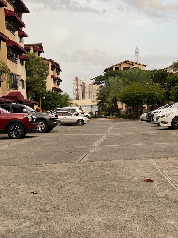Un estacionamiento con varios autos, rodeado de edificios con balcones y una palmera.