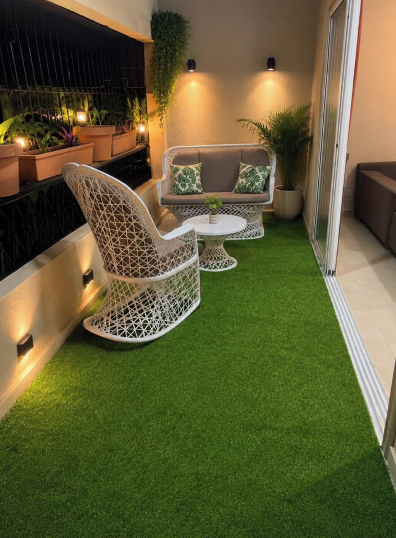 A small outdoor seating area with a white wicker chair and sofa, a round table, and artificial green turf.