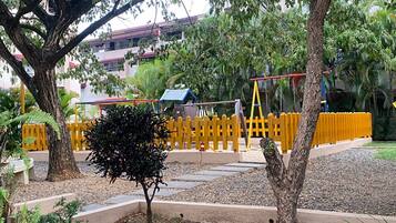 A playground with yellow fencing, a small tree, and a building with a red roof in the background.