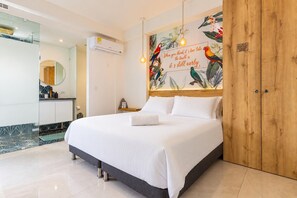 A hotel room with a bed, a wooden headboard, a wall mural with tropical birds, and a bathroom with a mirror and sink. - Utopia 5.East - Modern Loft•AC•Wi-Fi•Self Check-In (Medellín)