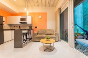 En moderne opholdsstue med et køkken, en sofa, et sofabord og udsigt til en balkon med planter.