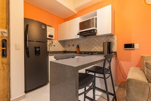 A compact kitchen with a refrigerator, microwave, and stove, featuring a herringbone tile backsplash and a small island with bar stools. - Utopia S.East – Quiet Loft•Wi-Fi•Self Check-In (Medellín)