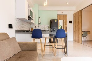 A modern kitchen with a refrigerator, microwave, and stove. There are two blue chairs and a sofa in the living area. - Utopía 3.West–Elegant 2BR•Wi-Fi•AC•Self Check-In (Medellín)
