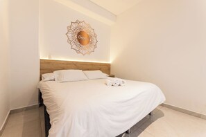 A neatly made bed with white linens and rolled towels, a wooden headboard, and a wall-mounted decorative piece. - Utopía 3.West–Elegant 2BR•Wi-Fi•AC•Self Check-In (Medellín)
