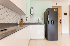 A kitchen with a black refrigerator, white cabinets, a herringbone tile backsplash, and a wooden door. - Utopía 3.West–Elegant 2BR•Wi-Fi•AC•Self Check-In (Medellín)