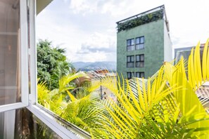 A window view of a building with a green facade and multiple windows, surrounded by lush green foliage. - Utopía 3.West–Elegant 2BR•Wi-Fi•AC•Self Check-In (Medellín)