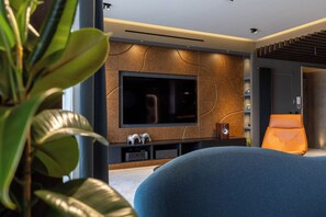 Una sala de estar moderna con un televisor de pantalla plana grande montado en una pared con textura, un sofá azul cómodo y una silla naranja pequeña.