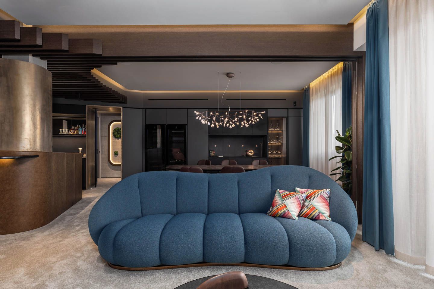 Een moderne woonkamer met een blauwe bank, een kroonluchter en een bar.