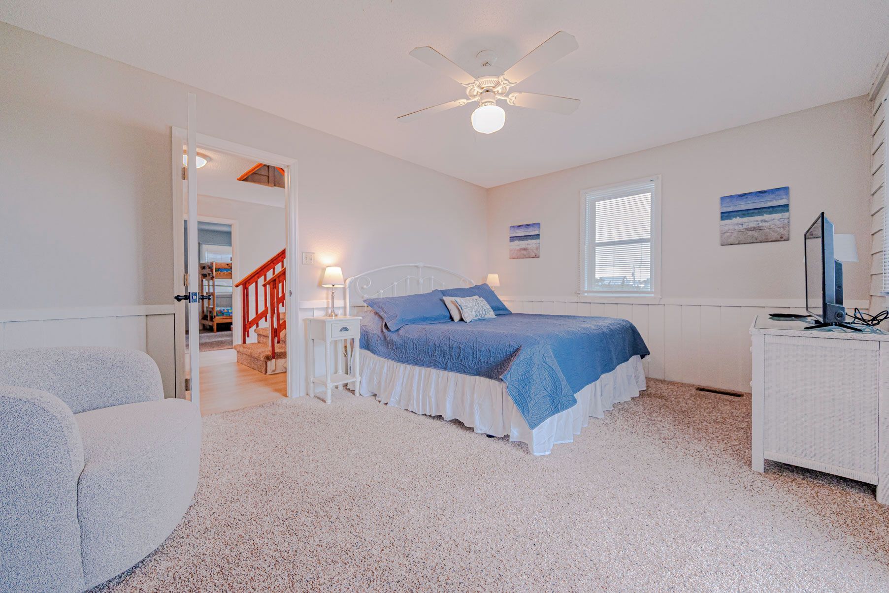 A bedroom with a bed, a desk, a chair, a ceiling fan, and a window.