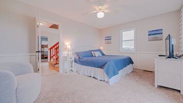 A bedroom with a bed, a desk, a chair, a ceiling fan, and a window.