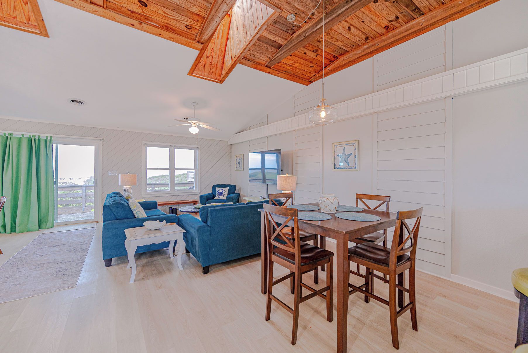 A spacious living area with a wooden ceiling, a dining table with chairs, a blue sofa, and a television.