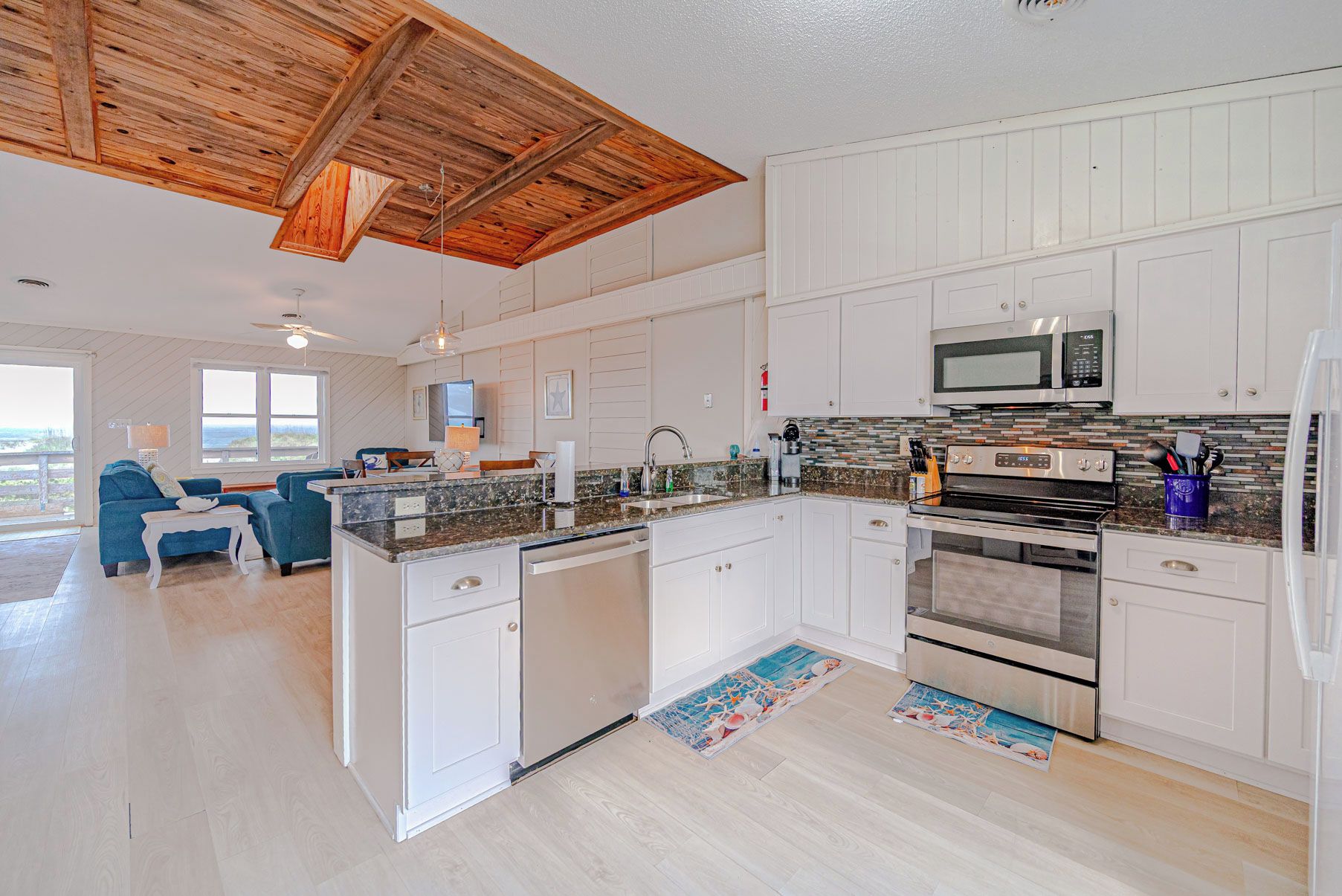 A modern kitchen with white cabinetry, a microwave, an oven, and a granite countertop.