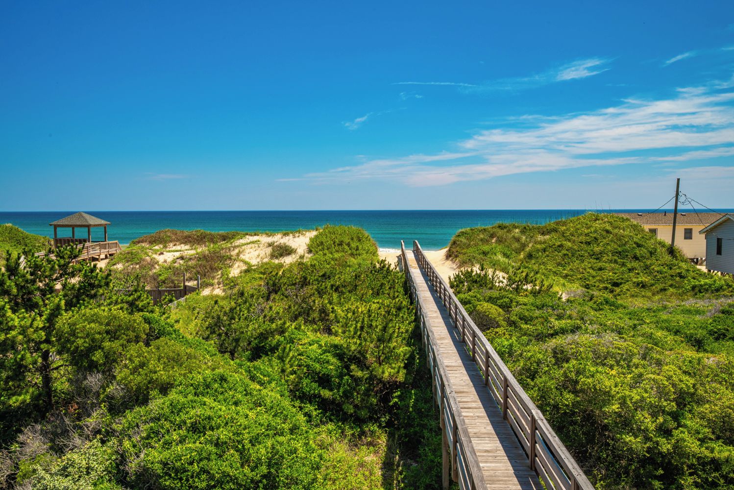 A wooden boardwalk leading to a beach with a gazebo and a small building.
