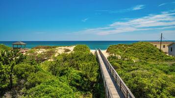 A wooden boardwalk leading to a beach with a gazebo and a small building.