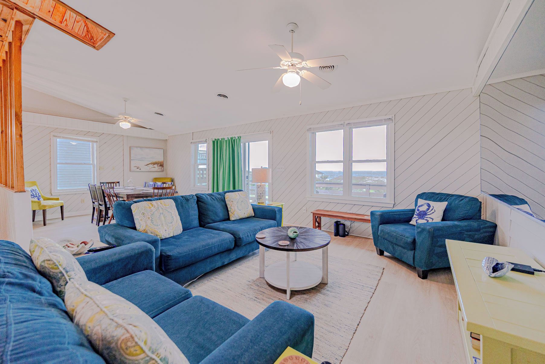 A spacious living room with a blue sofa set, a round coffee table, and a ceiling fan.