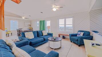 A spacious living room with a blue sofa set, a round coffee table, and a ceiling fan.