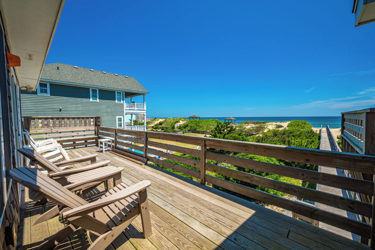 A wooden deck with lounge chairs overlooking a beach and ocean.