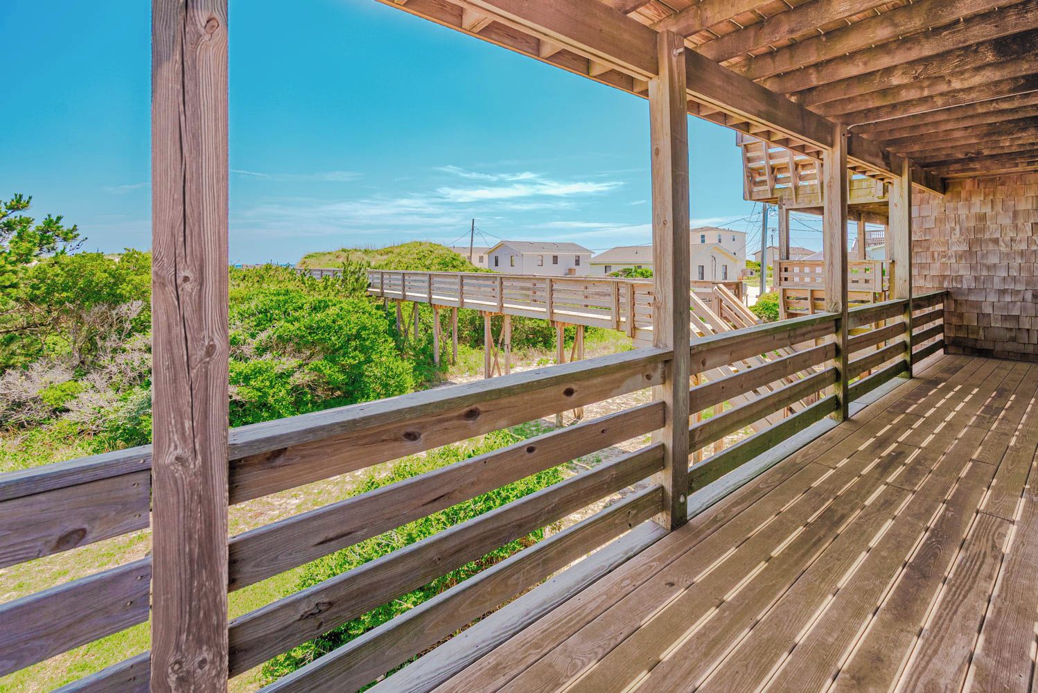 A wooden deck with a railing overlooking a beach and residential buildings.