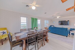 A dining area with a wooden table and chairs, a ceiling fan, and a television in the living room. - JL #367-A Double Dare - Oceanfront - Hot Tub (South Nags Head)