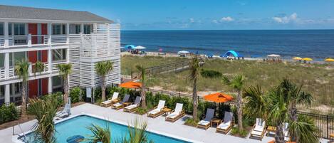 Un hotel con piscina, vistas a la playa y varios sillones de sol.