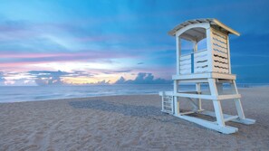 Ein Rettungsschwimmturm am Strand, im Hintergrund ein klarer Himmel und das Meer.