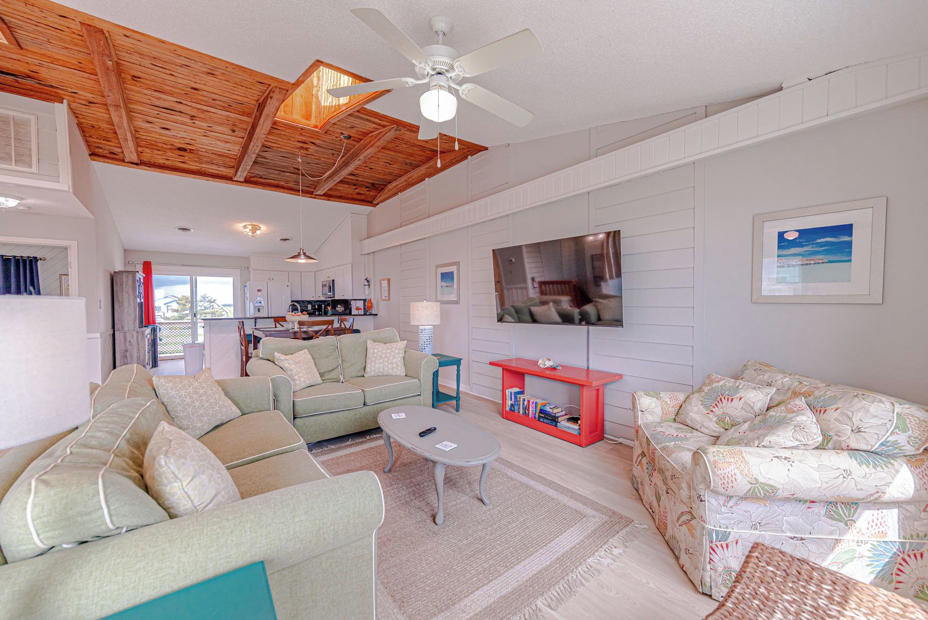 A spacious living room with a ceiling fan, a television, and a kitchen in the background.