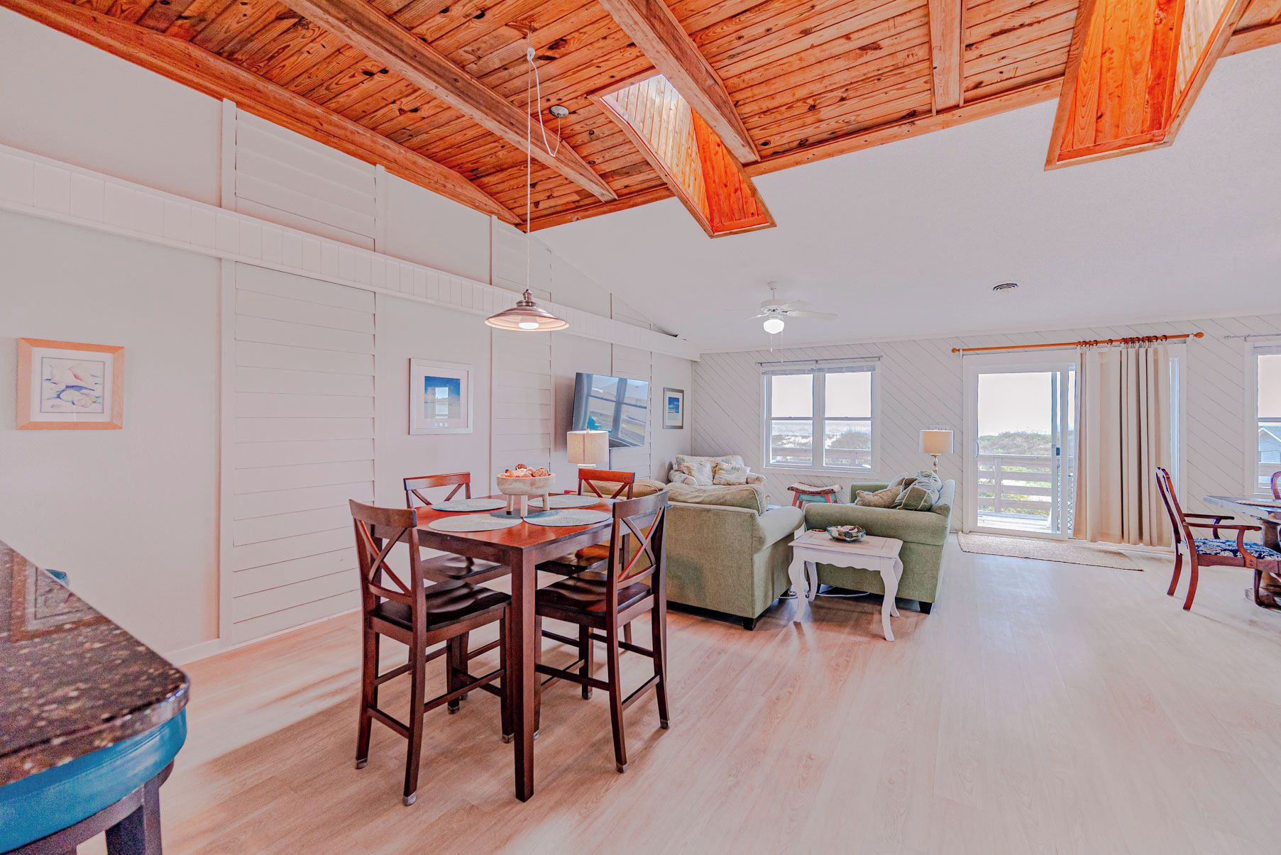 A spacious living area with a dining table, chairs, a sofa, and a large window offering a view.