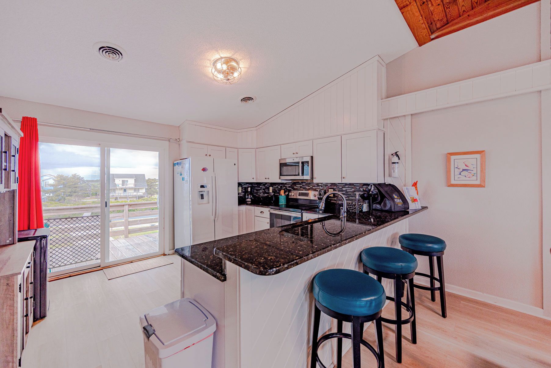 A modern kitchen with a central island, bar stools, a microwave, and a view through the sliding glass door.