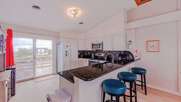 A modern kitchen with a central island, bar stools, a microwave, and a view through the sliding glass door.