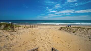 A beach with a wooden walkway leading to the water, a fence on the left, and a small structure on the right.