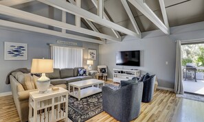 A modern living room with a sofa, coffee table, and a TV. There is a window with blinds, a rug, and a sign on the wall. - Dog Friendly Villa w/ Community Amenities (Hilton Head Island)