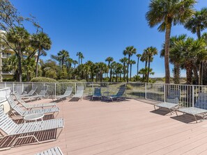 Una terrazza prendisole con poltrone reclinabili in metallo e ringhiera bianca, circondata da palme e un cielo azzurro intenso.