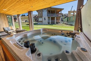 A hot tub with a stone exterior, a wooden ceiling, and a view of a residential area with houses and a clear sky. - Mountain Luxury Lodge w/Gondola Access 1099 (Steamboat Springs)