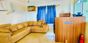 A living room with a sofa, a wooden reception desk, and a blue curtain. - Deluxe Srinivasa Home Stays (Hyderabad)