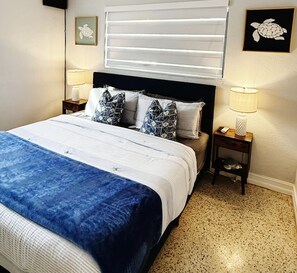Ein Bett mit blauer Bettdecke, zwei Nachttischlampen, ein Kopfteil und eine Wand mit einem gerahmten Bild.