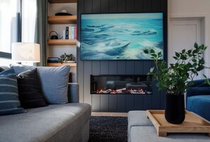 A modern living room with a flat-screen TV mounted above a fireplace, a sofa, and a coffee table with a plant. - 2 Turns - Revelstoke Vacations (Revelstoke)