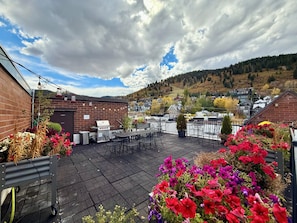 Eine Außenpatio mit Grill, Sitzgelegenheit und Blumenbeeten.