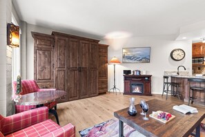 Eine moderne Küche mit Holzausstattung, ein Essbereich mit Tisch und Stühlen in rotem Karomuster, ein Kamin und eine Bar mit Sitzgelegenheiten.