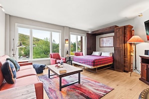 A spacious room with a bed, a sofa, a coffee table, and a view of greenery outside. - Main Street Condo - Walking Distance to Town Lift | Managed by Park City Lodging (Park City)
