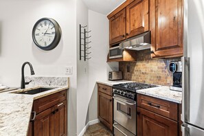 Una cucina con mobili in legno, un frigorifero in acciaio inossidabile, un forno a microonde, un fornello e una sveglia appesa al muro.