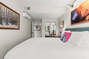 Una camera d'hotel con un letto grande, un dipinto raffigurante una foresta, un dipinto che mostra un canyon e una finestra con vista sugli alberi.