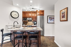 A modern kitchen with a central island, stainless steel appliances, wooden cabinets, and a clock on the wall. - Main Street Condo - Walking Distance to Town Lift | Managed by Park City Lodging (Park City)