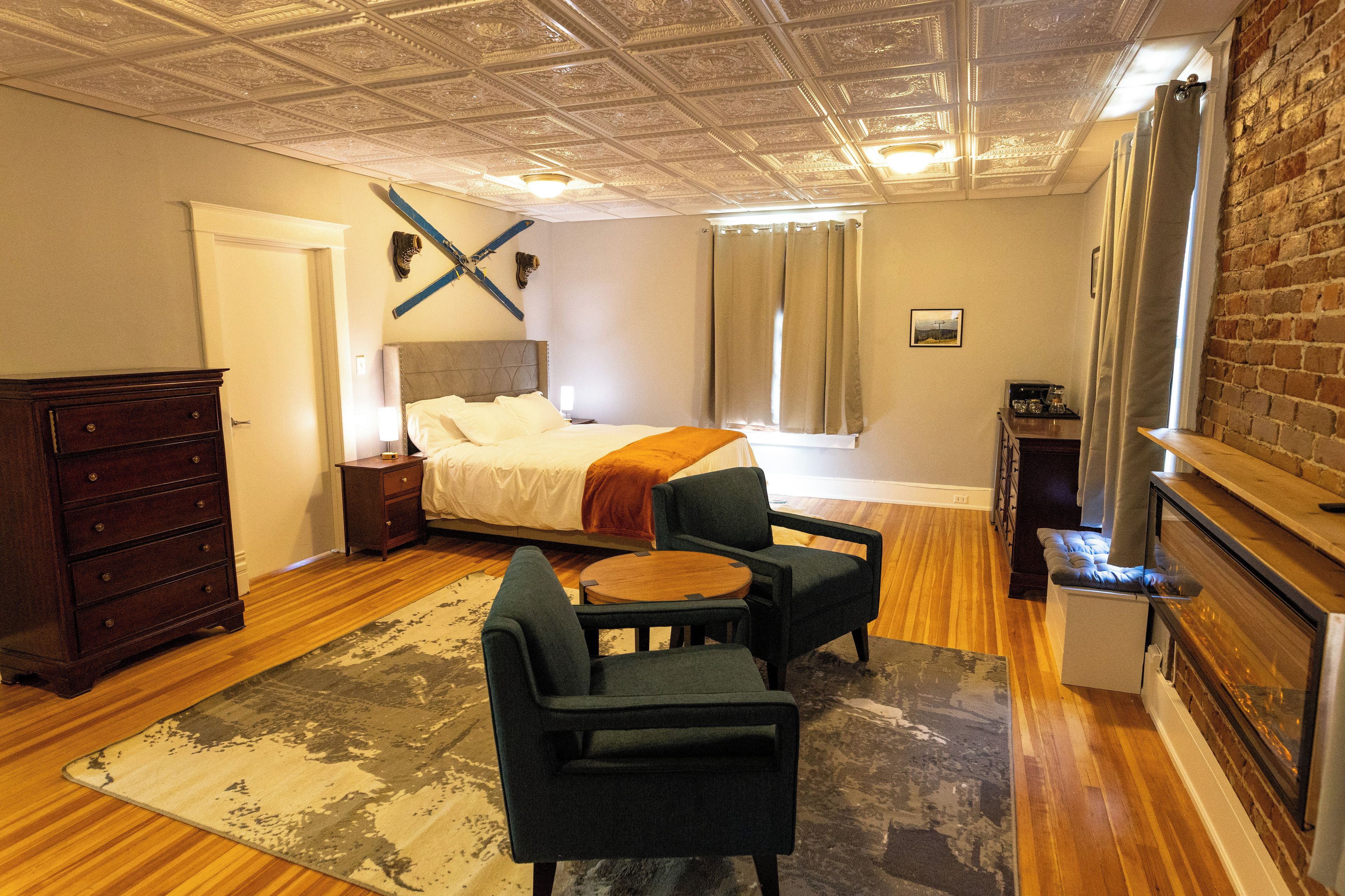Un dormitorio con cama, cómoda, escritorio, silla, chimenea y ventana con cortinas.
