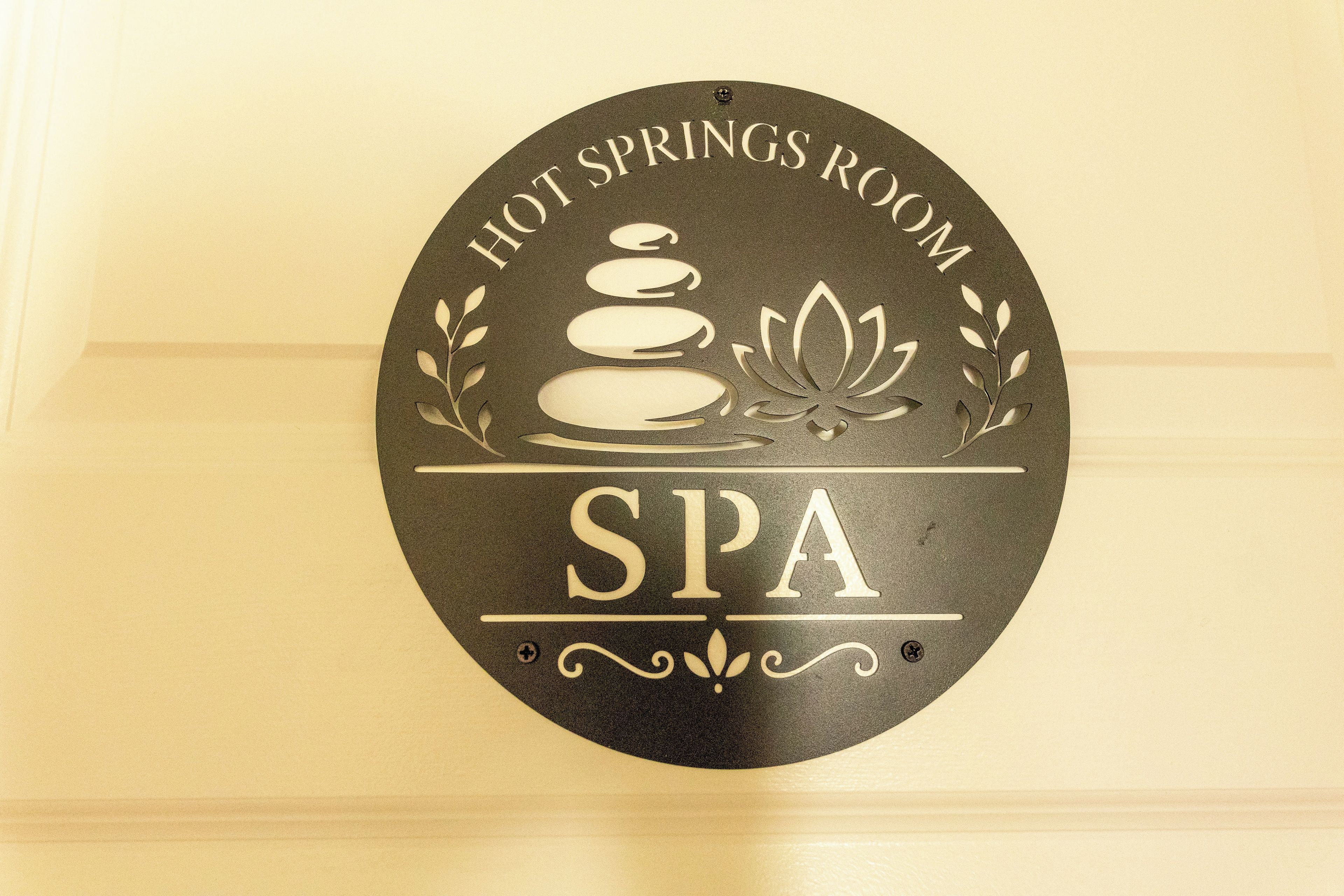 Un panneau circulaire portant les inscriptions « SALLE DE SOURCES CHAUDES » et « SPA », une pile de pierres et une fleur de lotus.