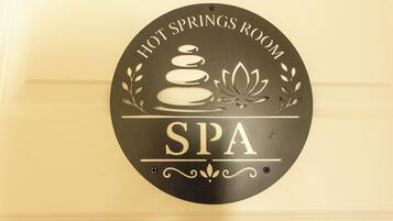 Un panneau circulaire portant les inscriptions « SALLE DE SOURCES CHAUDES » et « SPA », une pile de pierres et une fleur de lotus.